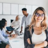 Blonde female executive posing with smile and arms crossed during brainstorm with managers Indoor portrait of european student spending time in hall with asian and african friends